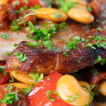 Close-up oven-roasted pork loin steaks with chorizo, peppers and beans in a honey glaze.