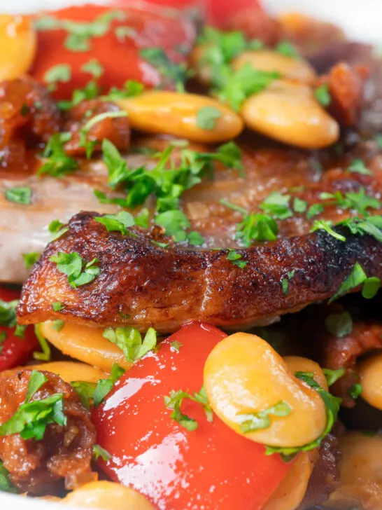 Close-up oven-roasted pork loin steaks with chorizo, peppers and beans in a honey glaze.