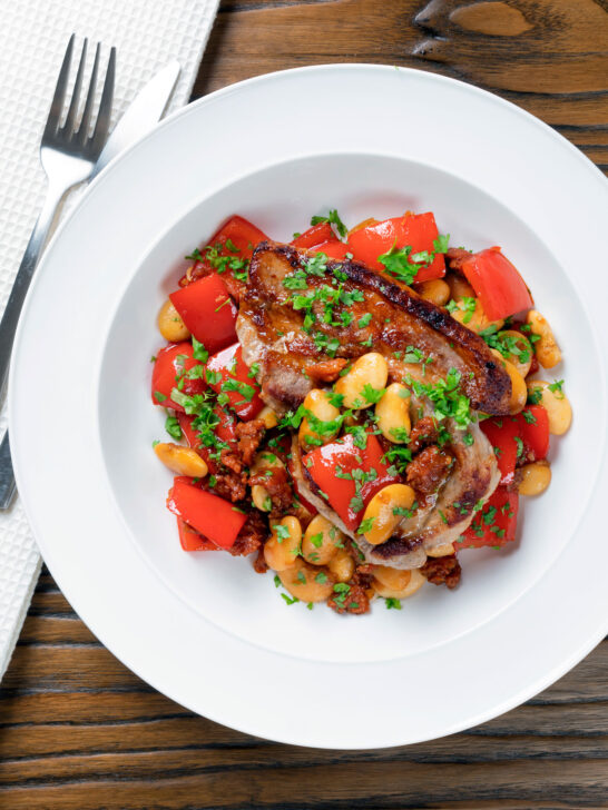 Overhead oven-roasted pork loin steaks with chorizo, peppers and beans in a honey glaze.