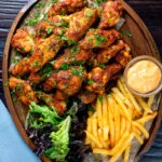 Overhead peri peri chicken wings with fries, spicy mayonnaise and salad.