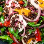 Close-up overhead French lentil salad with roasted peppers, goat's cheese and rocket featuring a title overlay.