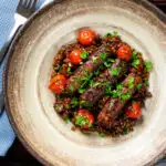 Overhead beef sausage and lentil casserole with cherry tomatoes featuring a title overlay.