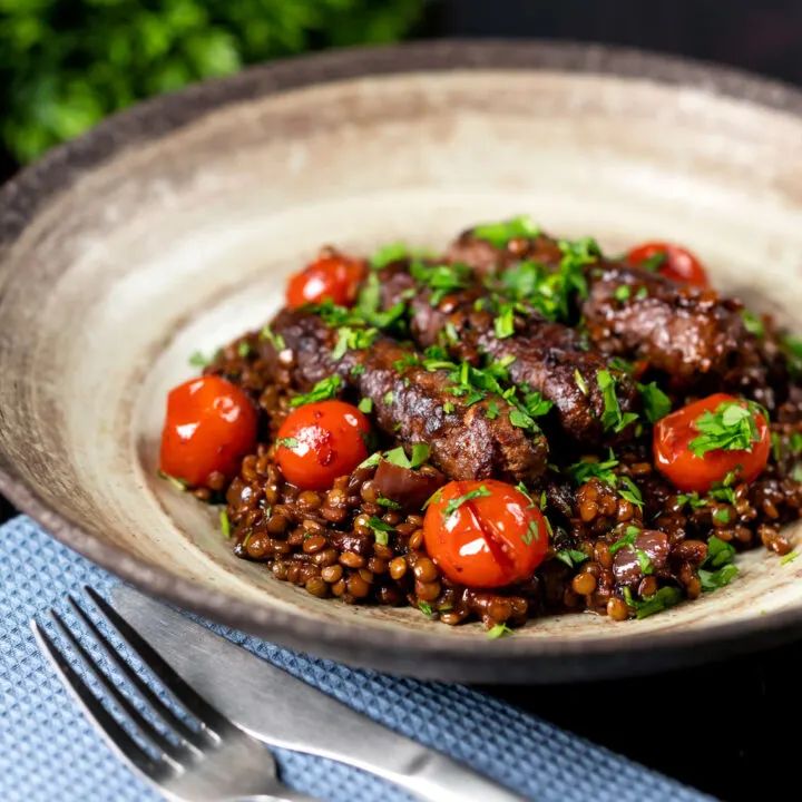 Sausage and lentil casserole with cherry tomatoes and fresh parsley in a large bowl.