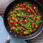 Overhead sausage and lentil casserole with cherry tomatoes in the cooking pan featuring a title overlay.
