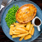 Overhead individual steak and Stilton pie with chips, peas and gravy.