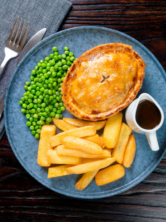 Overhead individual steak and Stilton pie with chips, peas and gravy.