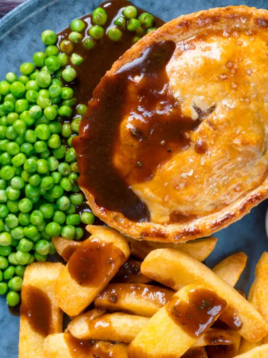 Overhead close-up steak and Stilton pie with chips, peas and gravy.