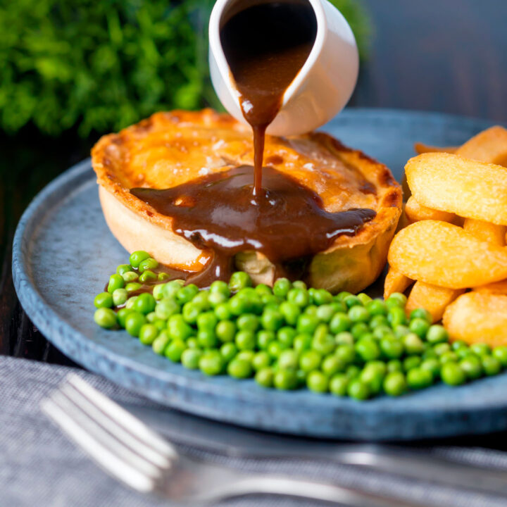 Individual Steak and stilton pie with chips, peas and gravy.