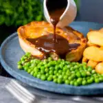 Rich gravy being poured over a steak and stilton pie served with chips and garden peas featuring a title overlay.