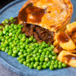 Cut open steak and stilton pie showing filling served with chips and garden peas featuring a title overlay.