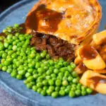 Cut open steak and stilton pie showing filling served with chips and garden peas featuring a title overlay.