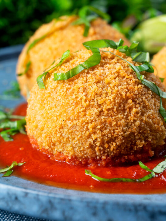 Close-up air fryer cooked arancini with an easy tomato sauce and fresh basil.
