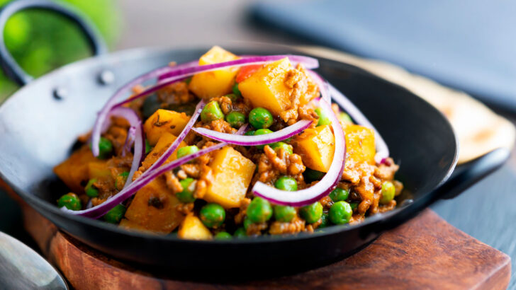 Indian Aloo keema or minced beef and potato curry with peas served in an iron karai.