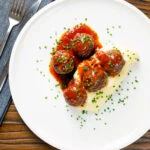 Overhead minced pork and black pudding meatballs with tomato sauce and mashed potato.