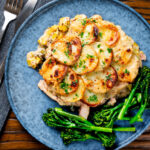 Overhead scalloped potato topped creamy chicken and leek hotpot with roasted tenderstem broccoli.