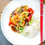 Overhead sweet and sour prawns stir-fry served with rice and spring onions.