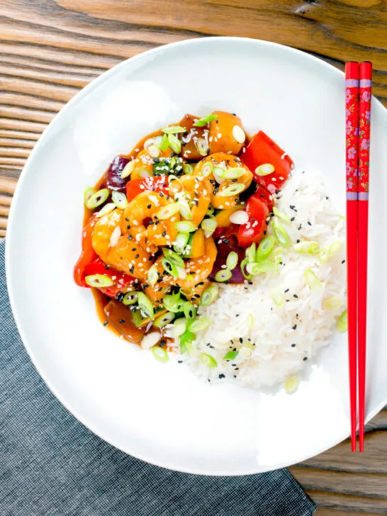 Overhead sweet and sour prawns stir-fry served with rice and spring onions.