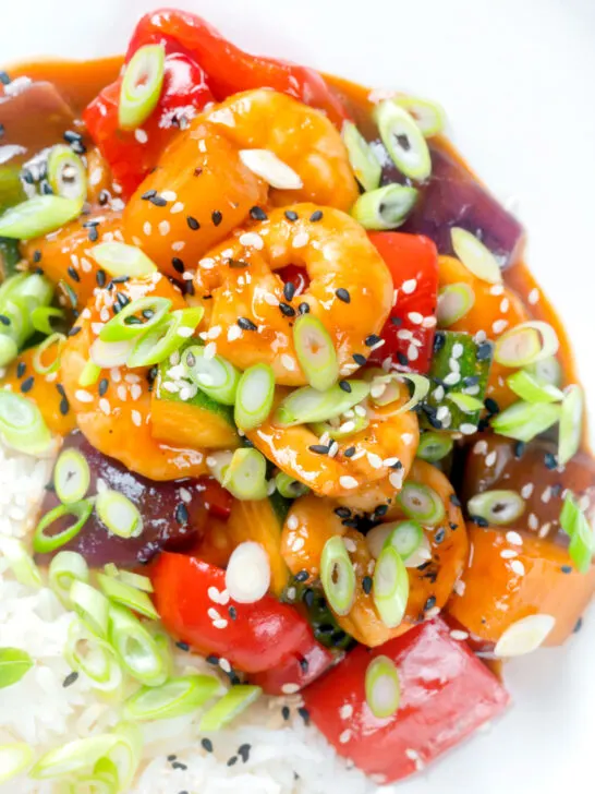 Close-up overhead sweet and sour prawns stir-fry served with rice and spring onions.