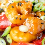 Close-up sweet and sour prawns stir-fry served with spring onions and sesame seeds.