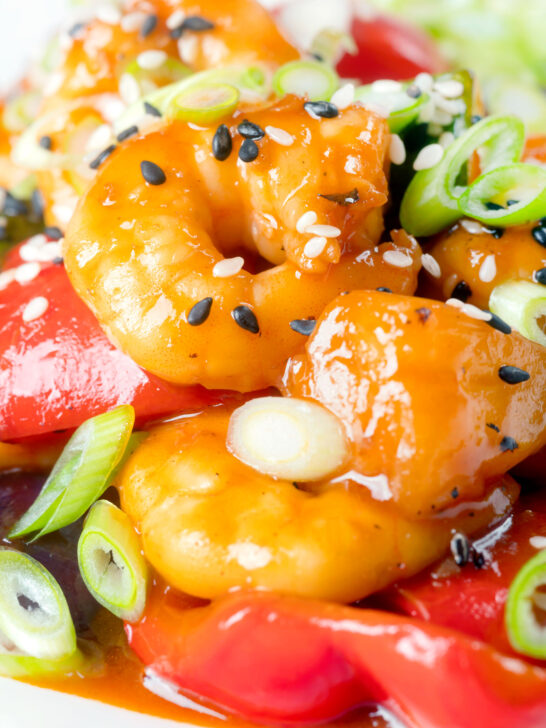 Close-up sweet and sour prawns stir-fry served with spring onions and sesame seeds.