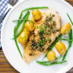 Overhead whole pan-fried lemon sole meuniere with a caper and butter sauce featuring a title overlay.