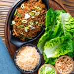 Overhead Chinese takeaway minced pork yuk sung with lettuce cups fried noodles and peanuts.