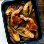 Roasted chicken legs, chicory and shallots in balsamic gravy in a roasting tin.