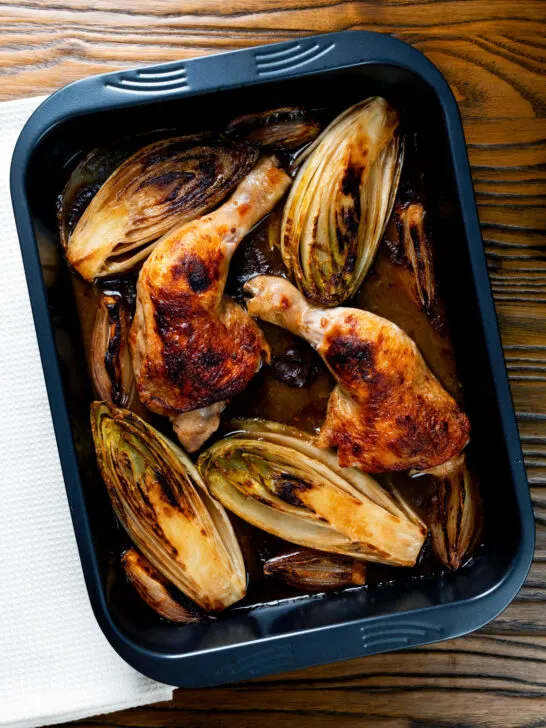 Roasted chicken legs, chicory and shallots in balsamic gravy in a roasting tin.