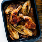 Roasted chicken legs, chicory and shallots in balsamic gravy in a roasting tin featuring a title overlay.
