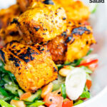 Salmon tikka served with a spicy cucumber salad with tomato, chilli and toasted peanuts featuring a title overlay.