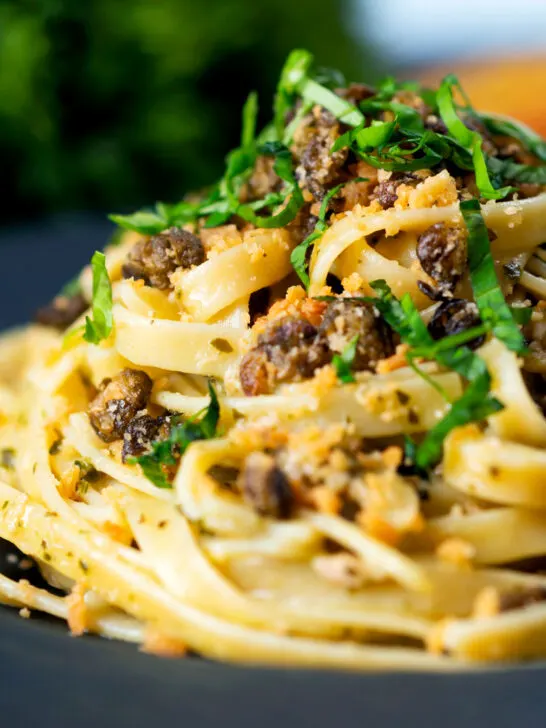 Close-up tuna pesto fettuccini with crispy capers, golden breadcrumbs and fresh basil.