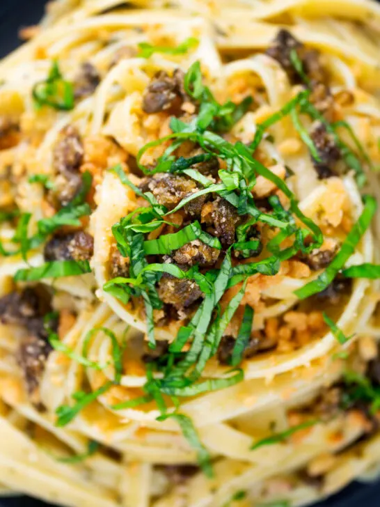 Overhead close-up tuna pesto fettuccini with crispy capers, golden breadcrumbs and fresh basil.