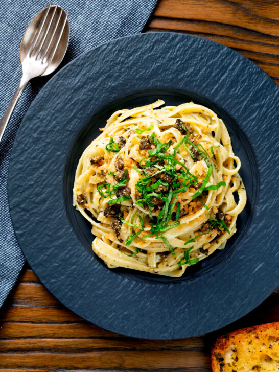 Overhead tuna pesto pasta with crispy capers, golden breadcrumbs and fresh basil.