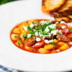 Spanish chorizo and butterbean stew with crumbled feta cheese and parsley featuring a title overlay.