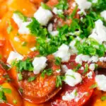 Close-up Spanish chorizo and butterbean stew with crumbled feta cheese and parsley.