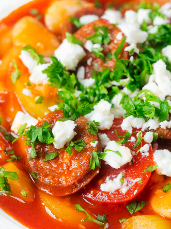 Close-up Spanish chorizo and butterbean stew with crumbled feta cheese and parsley.