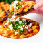 Chorizo and butter bean stew with crumbled feta cheese being eaten with toasted bread.