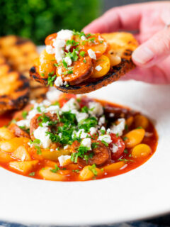 Chorizo and butter bean stew with crumbled feta cheese being eaten with toasted bread.