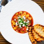 Overhead Spanish chorizo and butterbean stew with crumbled feta cheese and parsley.