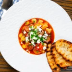 Overhead Spanish chorizo and butterbean stew with crumbled feta cheese and parsley.