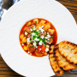 Overhead Spanish chorizo and butterbean stew with crumbled feta cheese and parsley featuring a title overlay.