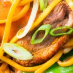Close-up duck breast chow mein stir fry with noodles, carrots and runner beans.