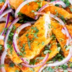 Close-up overhead fish finger and butter bean curry served with red onion and coriander.