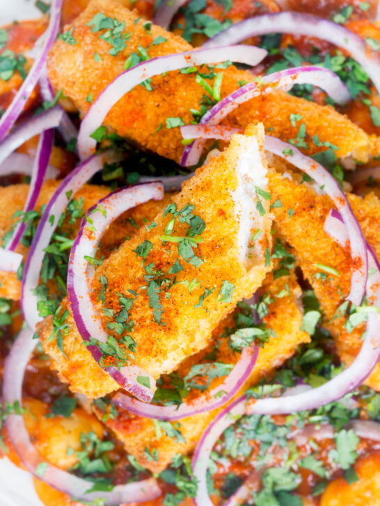 Close-up overhead fish finger and butter bean curry served with red onion and coriander.