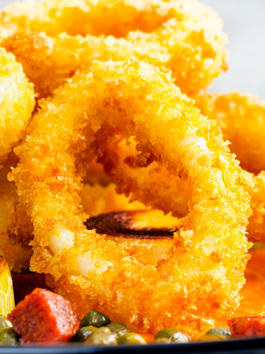 Close-up fried calamari rings with romesco sauce, leeks, chorizo and capers.