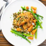 Overhead lemon and caper chicken piccata served with asparagus and carrots.