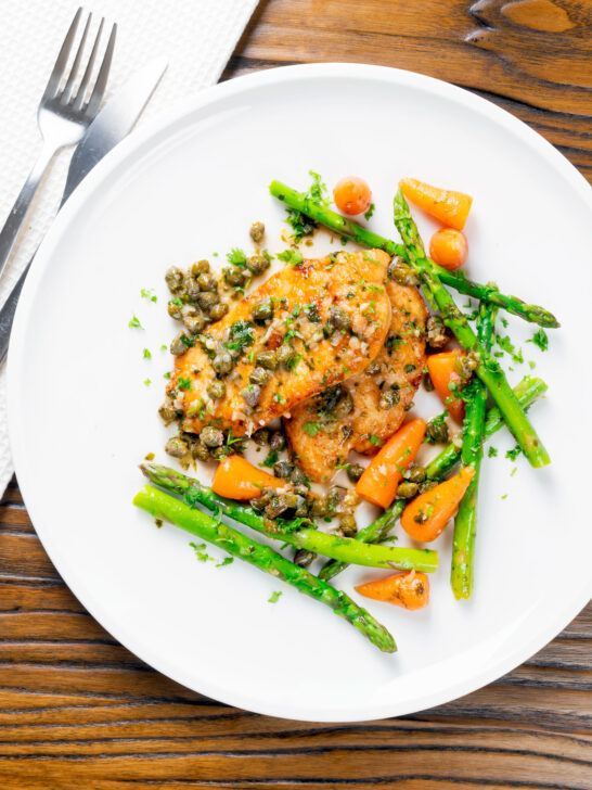 Overhead lemon and caper chicken piccata served with asparagus and carrots.