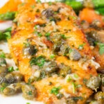 Close-up golden lemon and caper chicken piccata served with asparagus and carrots.