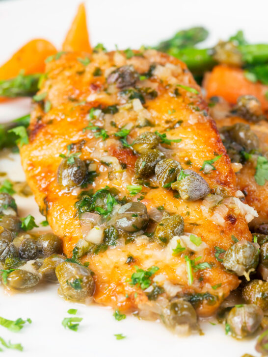 Close-up golden lemon and caper chicken piccata served with asparagus and carrots.