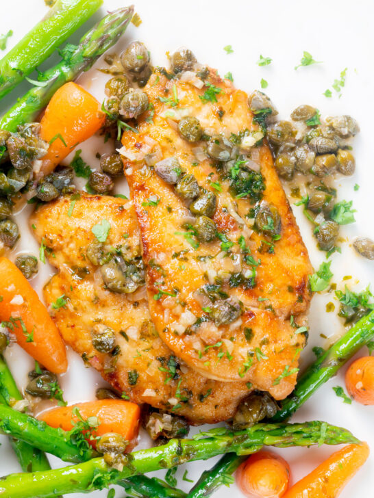 Overhead close-up lemon and caper chicken piccata served with asparagus and carrots.